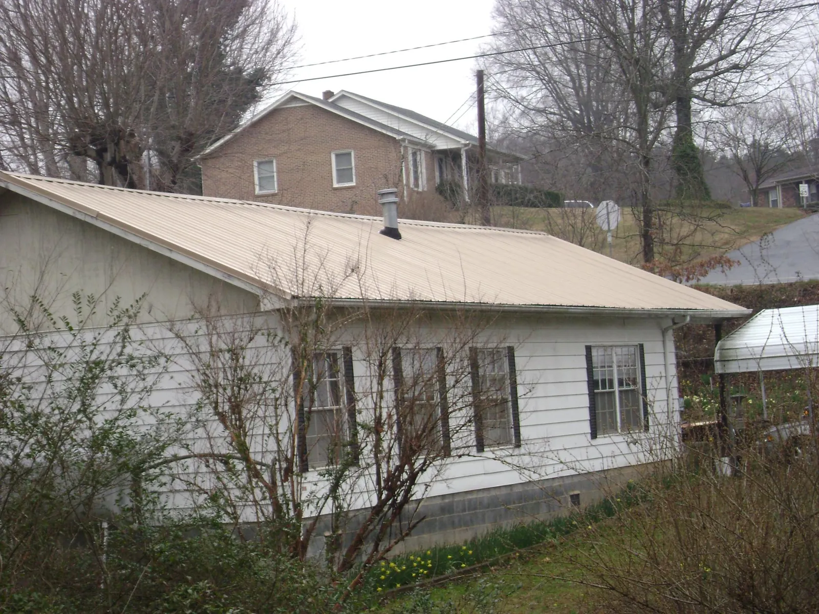 Tan metal roof on a white sided house set into a hillside — Commercial Roofing by Roofing Brothers in Midland